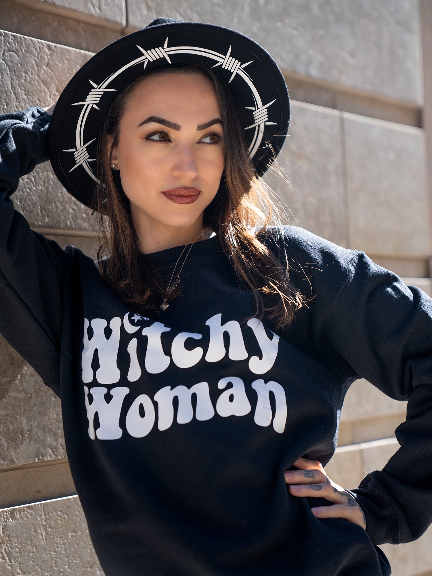 Janice Danger wearing a black wide brim felt hat with Barbed Wire white graphics and the Witchy Woman black crewneck sweatshirt. 