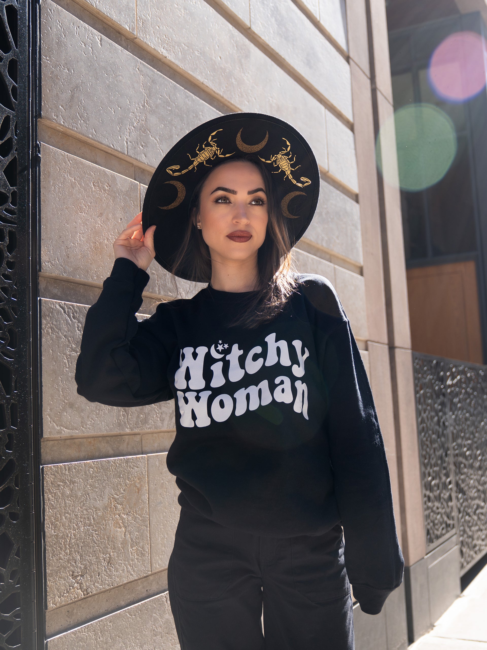 Janice Danger wearing a black and gold wide brim felt hat featuring scorpions and moons. Photographed outside in the West Village NYC