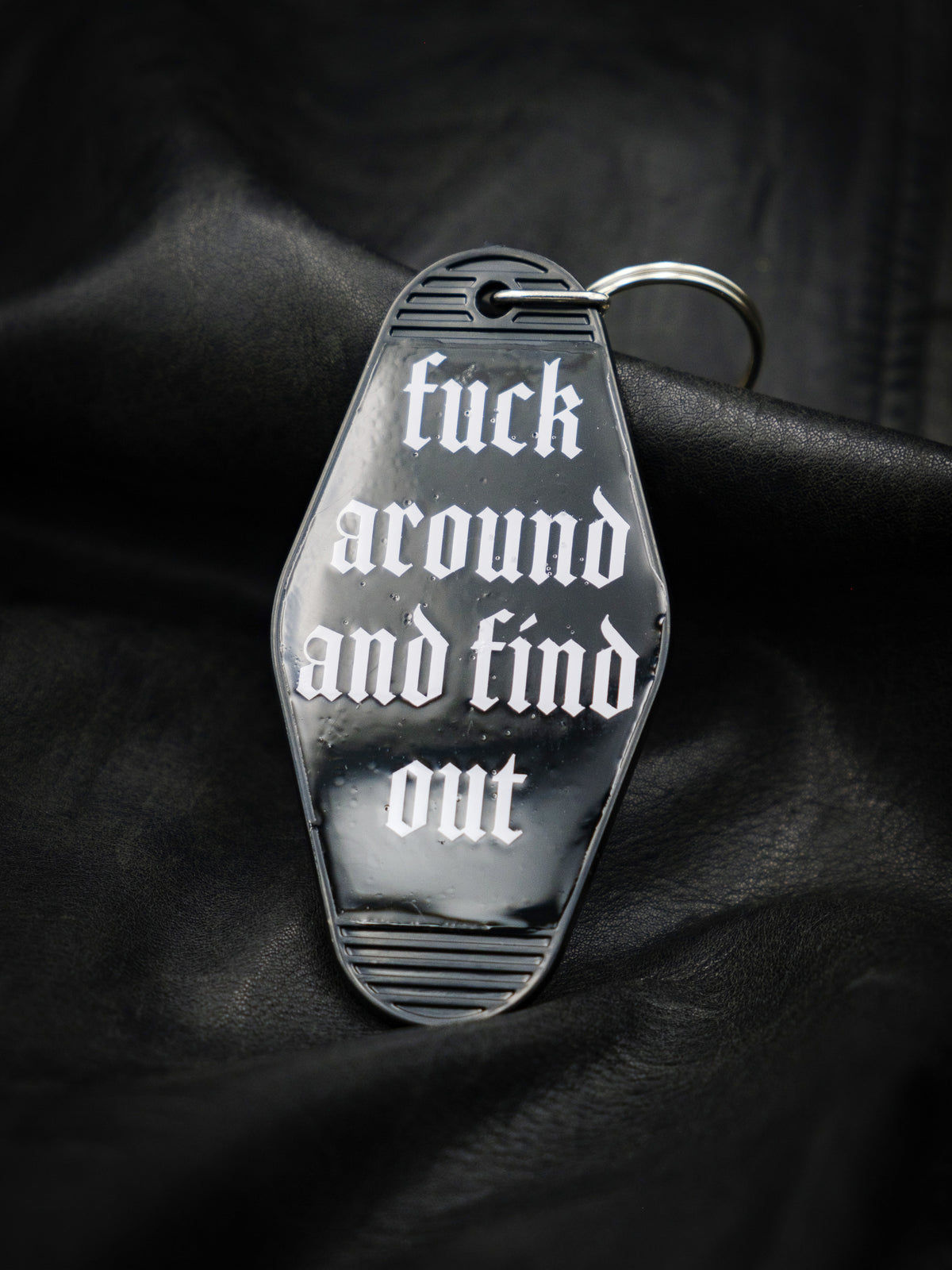 black motel style keychain reads Fuck Around and Find Out in an old english type font in white. 