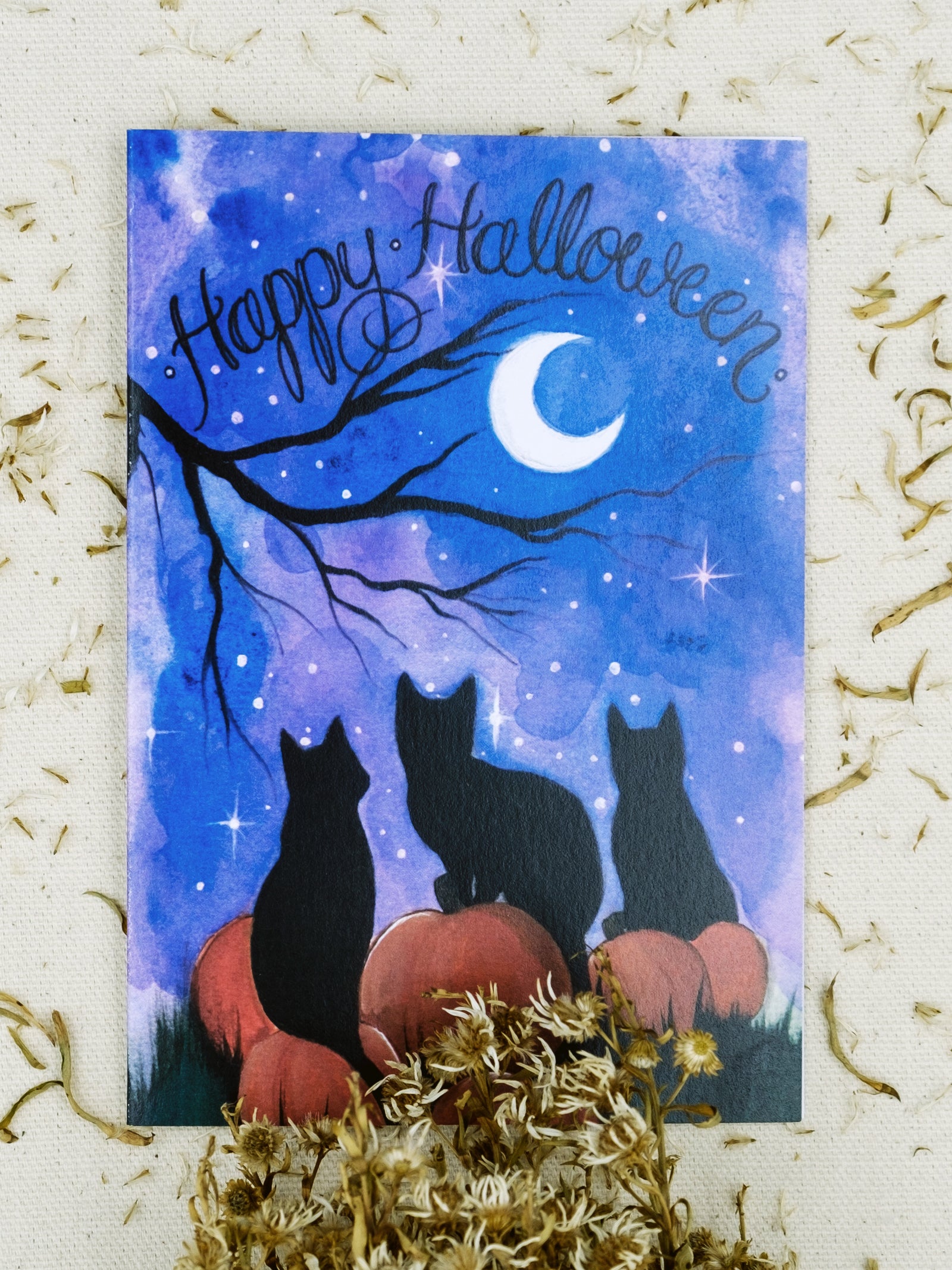 Happy Halloween Greeting card featuring three black cats in a pumpkin patch at night. 