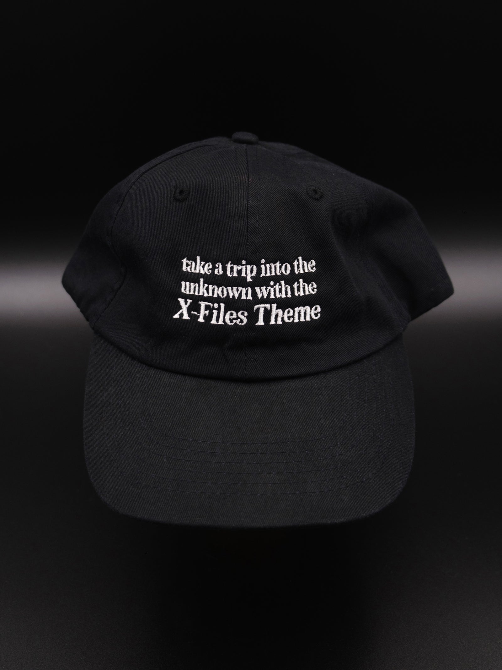 black hat with white embroidered text reads "take a trip into the unknown with the X-Files theme"