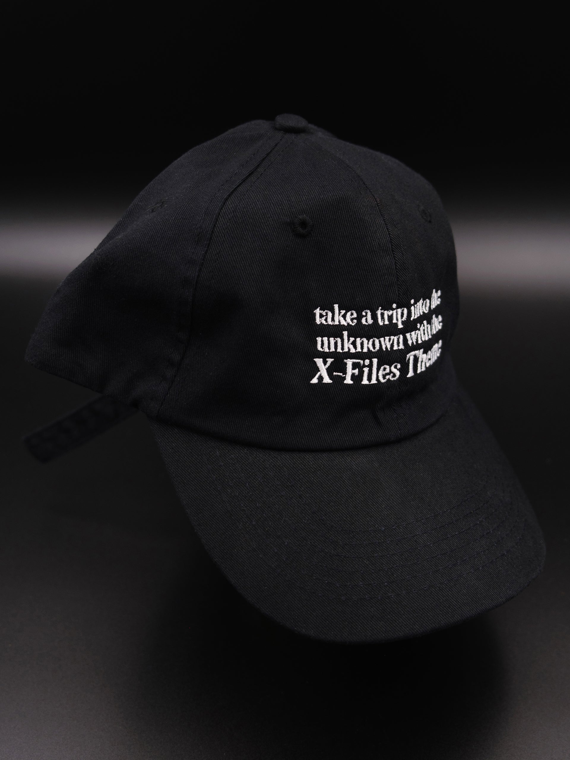 black hat with white embroidered text reads "take a trip into the unknown with the X-Files theme"