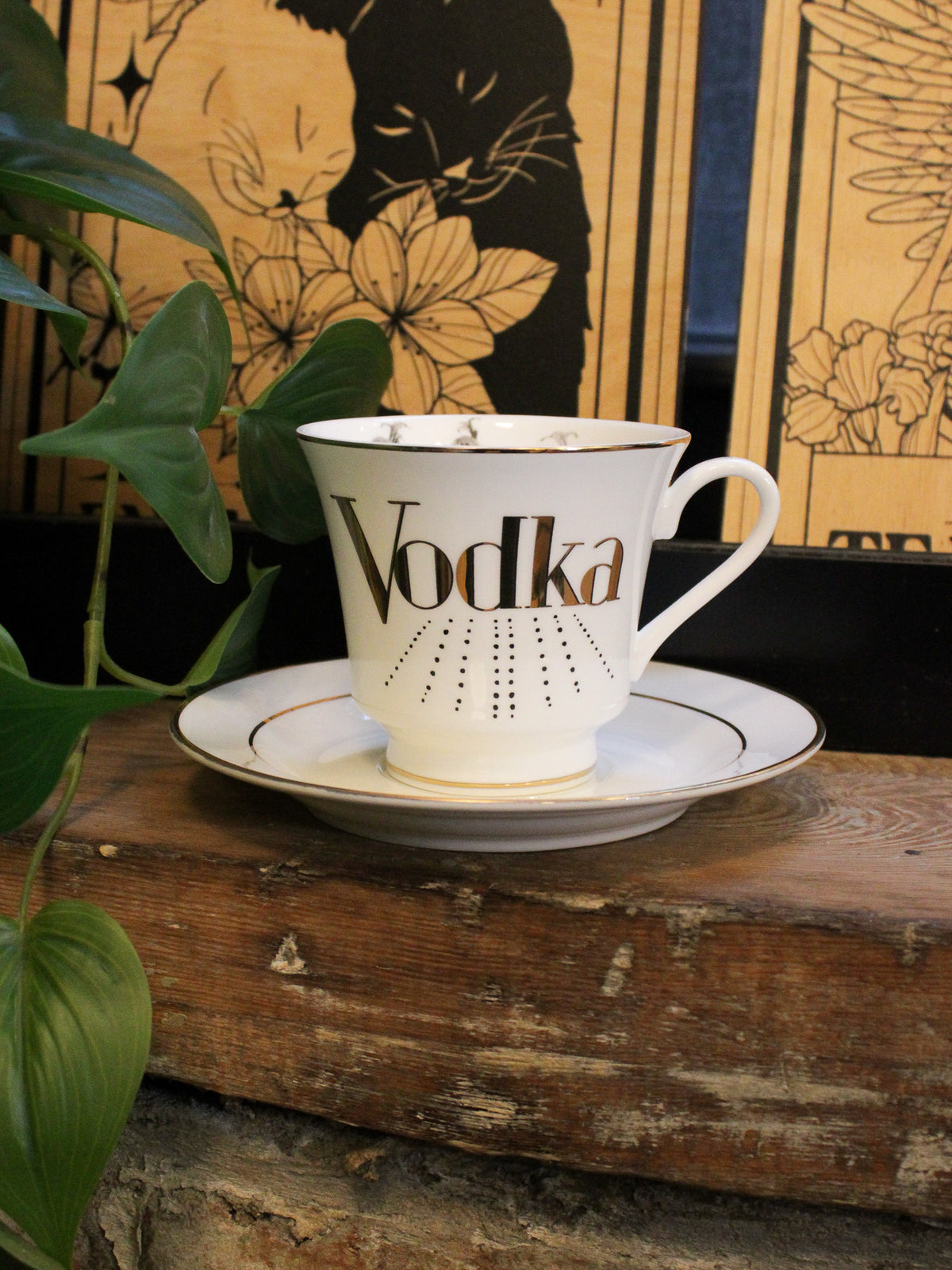 White china teacup with gold detailing reads &quot;vodka&quot; with  gold trim. 