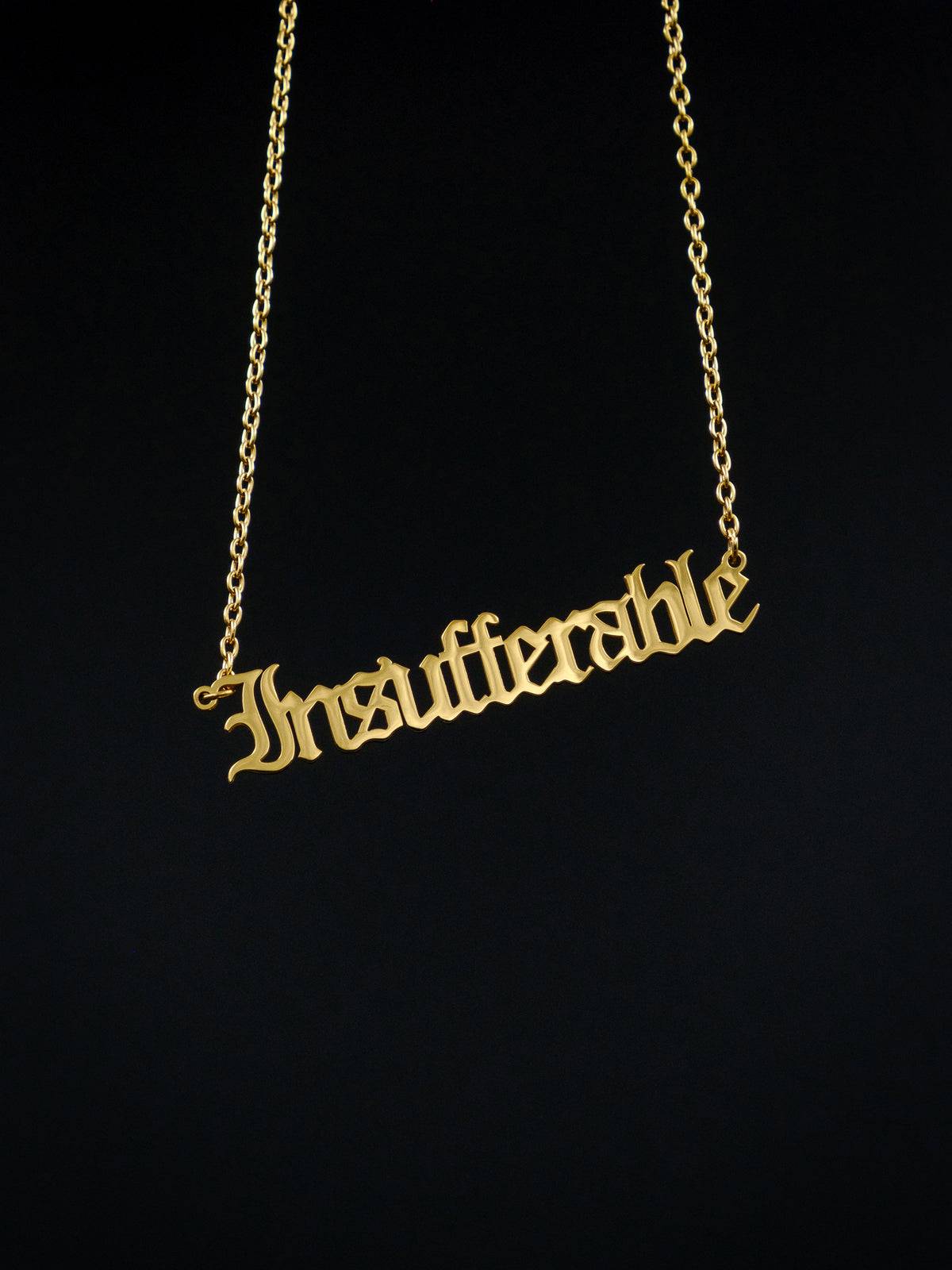 gold nameplate style necklace against a black background reads &quot;insufferable&quot; in old english style font