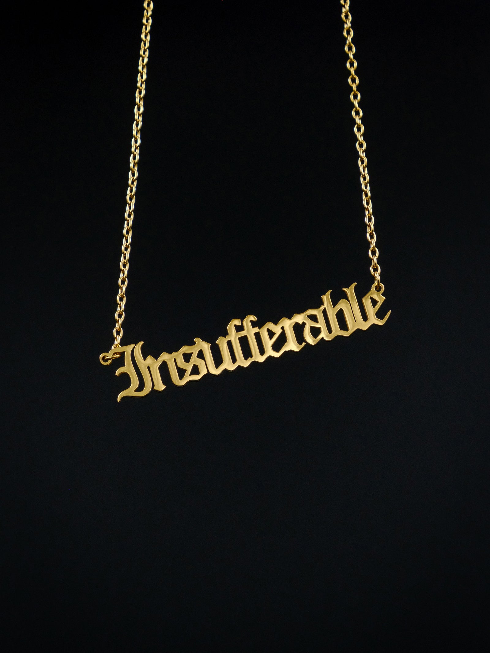 gold nameplate style necklace against a black background reads "insufferable" in old english style font