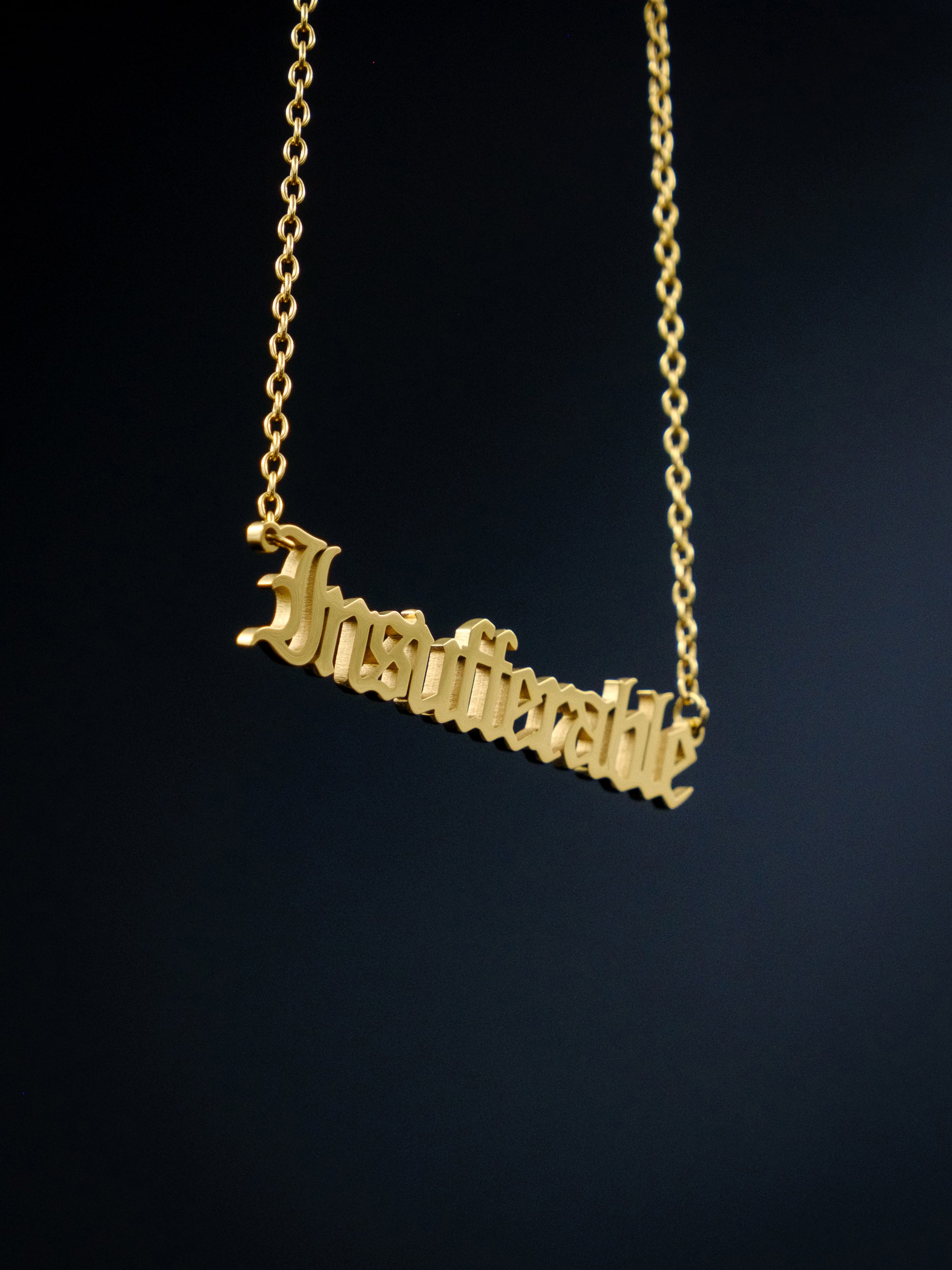 gold nameplate style necklace against a black background reads "insufferable" in old english style font