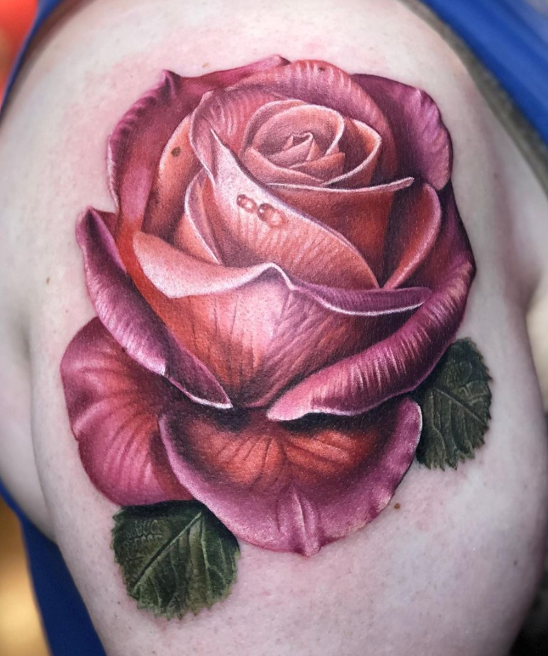 Photorealistic Pink Rose and leaves arm tattoo by Megan Massacre. This detailed, color-realism tattoo features petal creases and dew drops.