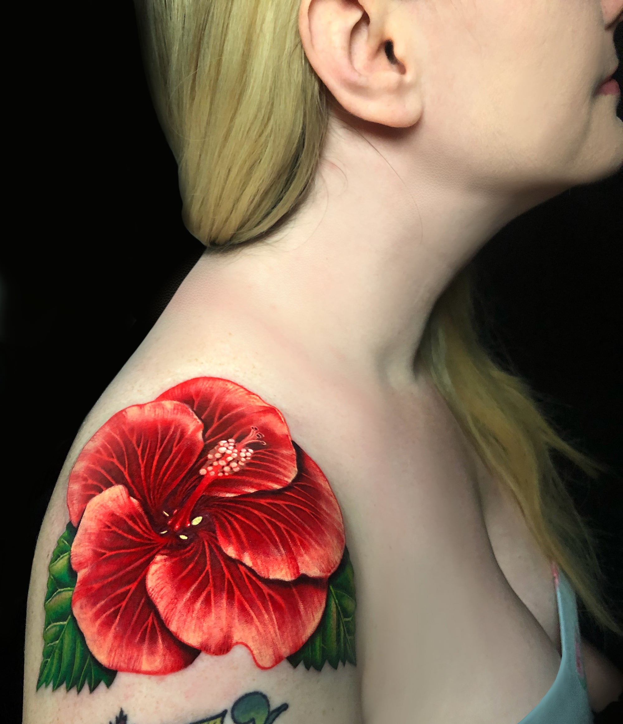 Color realism red hibiscus flower shoulder tattoo by Megan Massacre at Grit N Glory in New York City.