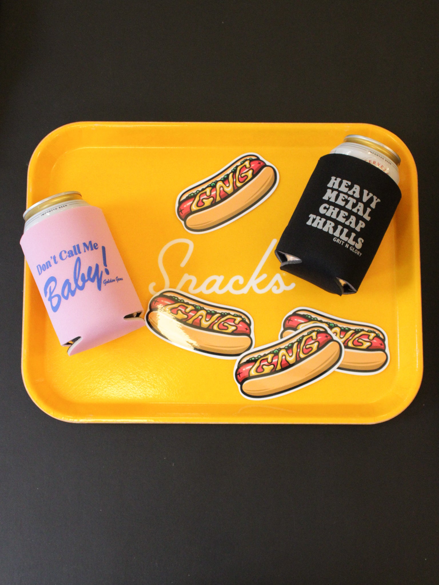 Yellow snack tray with hotdog GNG stickers and two cans with koozies.