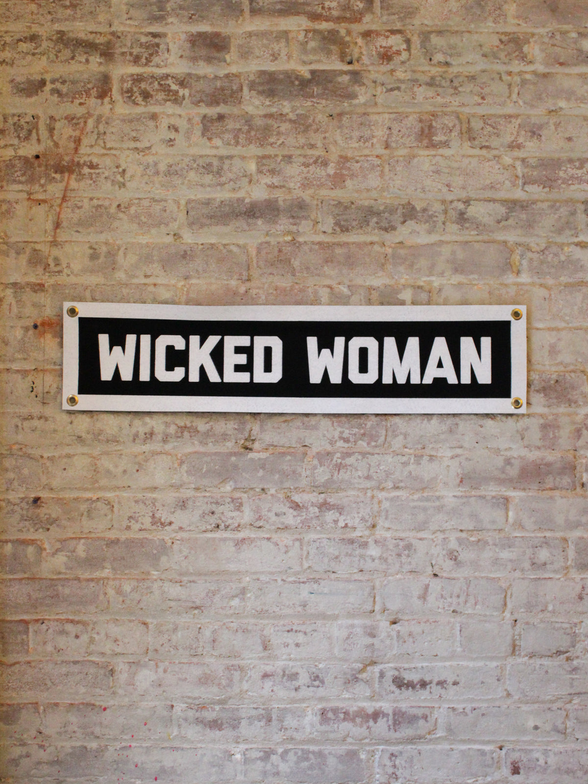 black and white rectangle banner with 4 gold grommets reads &quot;wicked woman&quot;